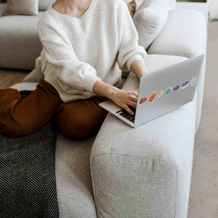 a woman sitting on a couch using a laptop with stickers from the seven chakras watercolor sticker sheet