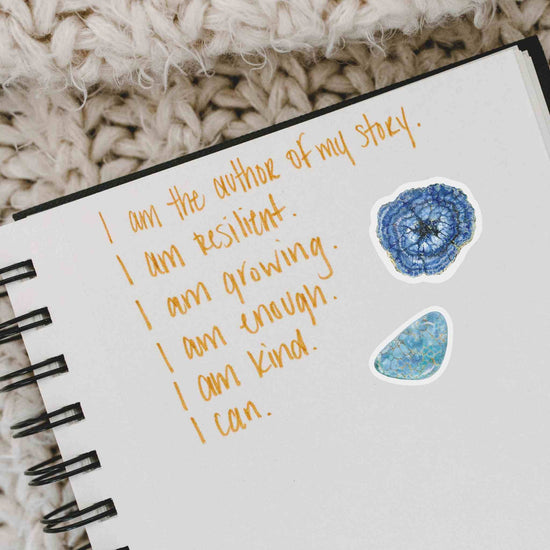 an open notebook with a handwritten note with azurite and turquoise stickers