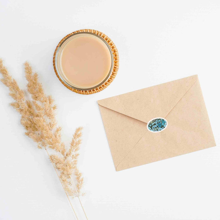 a cup of coffee next to an envelope with a turquoise sticker on it