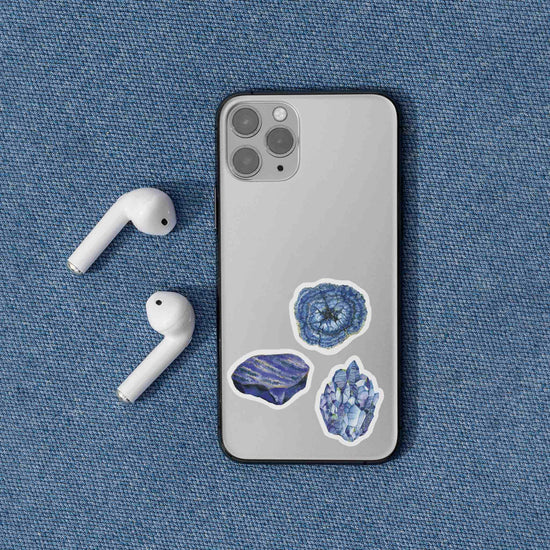 a cell phone with lapis lazuli and azurite stickers next to a pair of ear buds