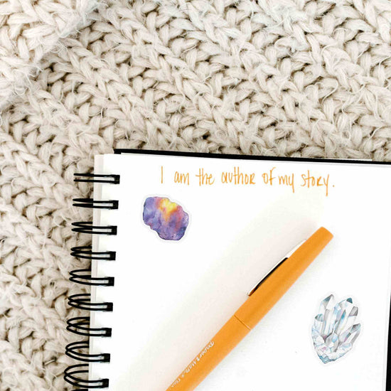 a notepad with a pen on top of it with watercolor crystal stickers for the crown chakra