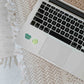 a laptop computer sitting on top of a table with stickers from the heart chakra watercolor crystal sticker set