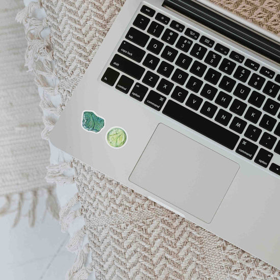 a laptop computer sitting on top of a table with stickers from the heart chakra watercolor crystal sticker set