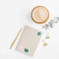 a desk with a notebook with stickers from the heart chakra watercolor crystal sticker set, pen, and a cup of coffee