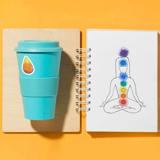 a personalized to go cup with an amber crystal sticker next to a notebook with a drawing of a woman