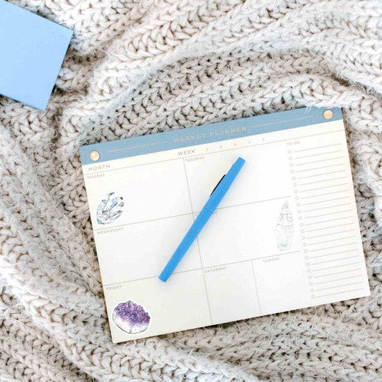 a blue pen sitting on top of a calendar with watercolor crystal stickers for the crown chakra