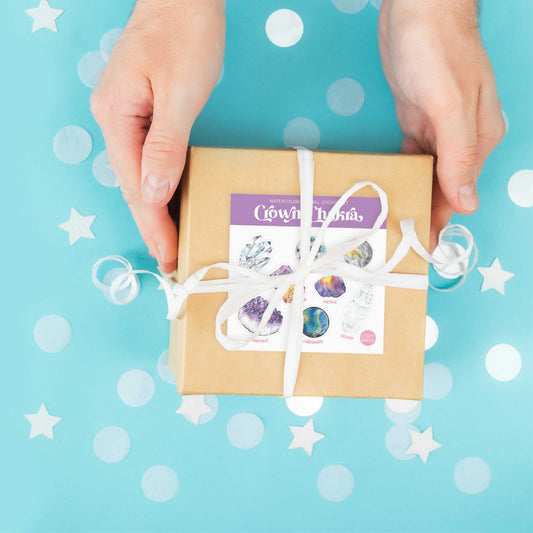 a person holding a brown box with a white ribbon with the watercolor crystal sticker set for the crown chakra