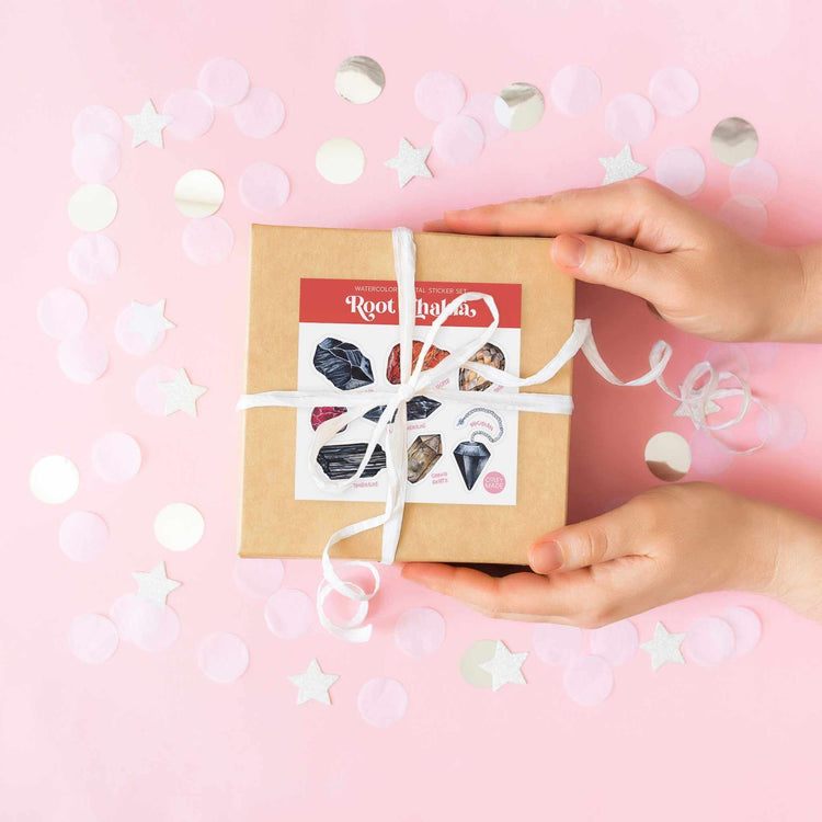 a person's hands holding a brown box with white ribbon with the root chakra watercolor crystal sticker set