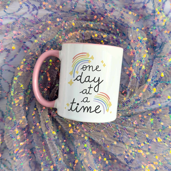 a pink coffee mug with a one day at a time written on it