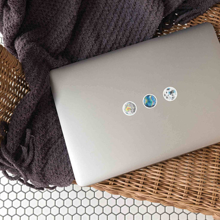 a laptop computer sitting on top of a wicker basket with stickers from the watercolor crystal sticker set for the crown chakra