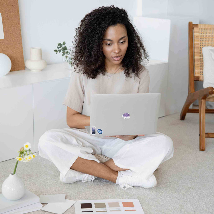 a woman sitting on the floor using a laptop with iolite and amethyst stickers on it