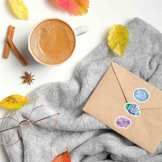 a cup of coffee and an envelope with fluorite, calcite and ametrine stickers on a blanket