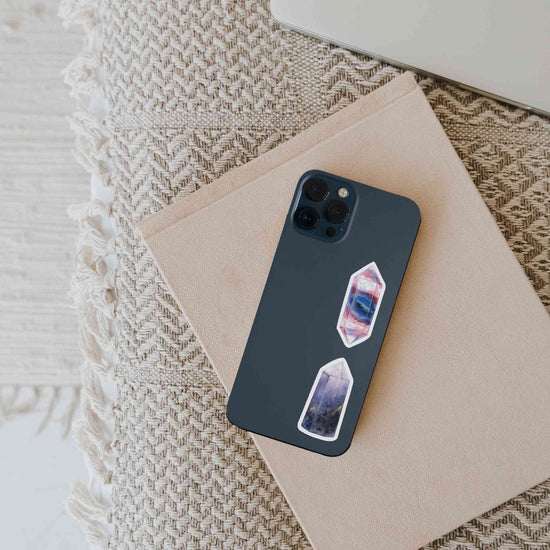 a cell phone sitting on top of a notebook with fluorite and iolite stickers on it