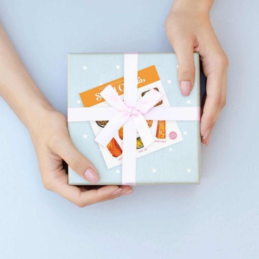 a person holding a gift box with a white ribbon with the sacral chakra watercolor crystal sticker set