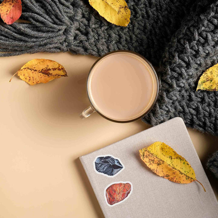 a cup of coffee next to a book with autumn leaves on it and stickers from Root Chakra Crystal Sticker Set