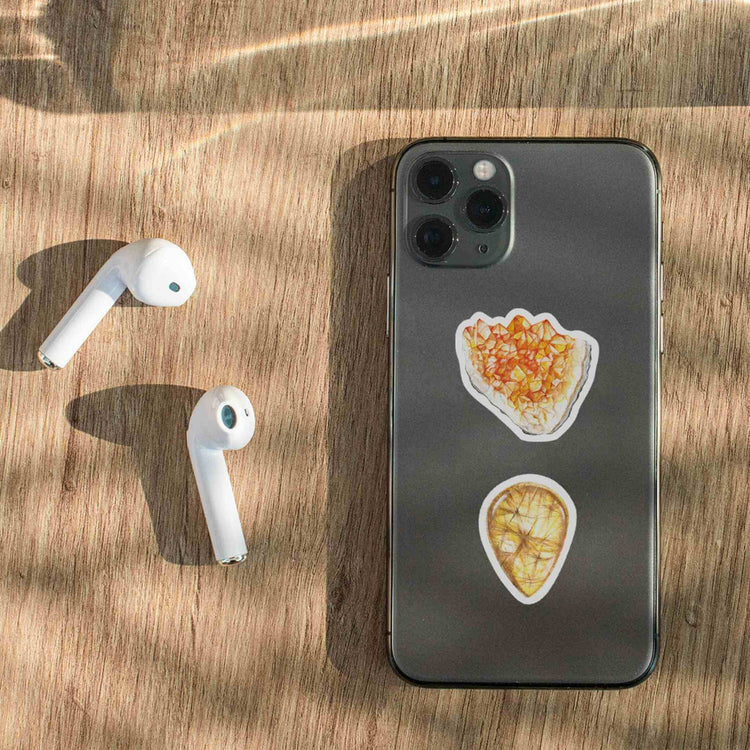 an iphone with citrine and rutliated quartz stickers on it next to ear buds
