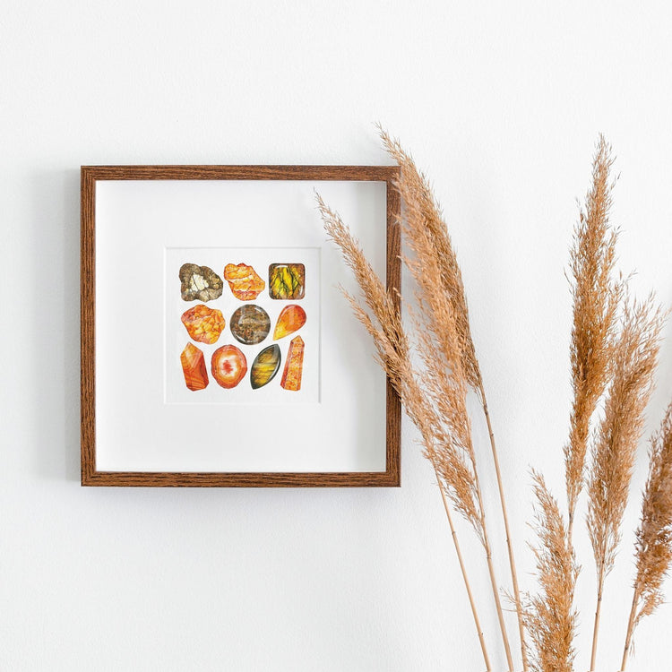 a white wall with a wooden frame holding the sacral Chakra Watercolor Crystal Art Print next to a plant